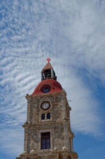 An ancient bell tower with red roof and clock in front of a blue sky with clouds, Roloi Clock