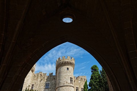 View through a stone arch to a medieval castle with tower under a blue sky, Grand Master's Palace,