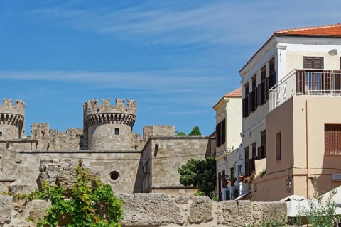 Castle with medieval stone towers next to a Mediterranean building under a blue sky, Grand Master's