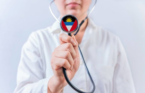 Female doctor holding stethoscope with Antigua and Barbuda flag. National health system of Antigua