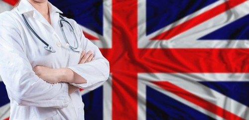 Doctor with crossed arms on United Kingdom flag. United Kingdom health and care concept. Female