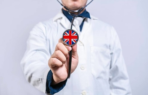 Doctor hands holding stethoscope with United Kingdom flag. United Kingdom health and care concept