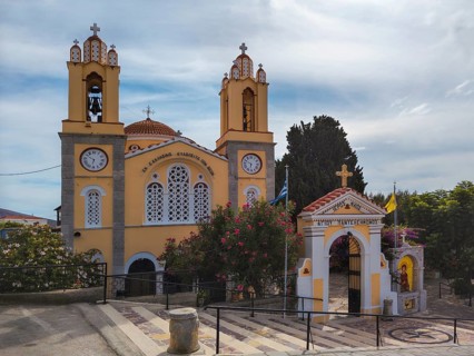 Yellow church with bell towers and flowers under a blue sky, Greek Orthodox Church of Saint