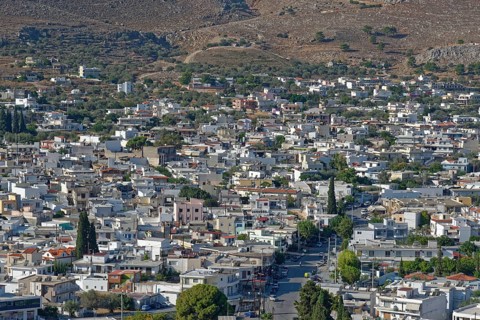 Town of Archangelos with densely built blocks of houses and green trees on hilly terrain,