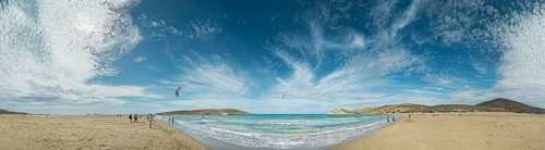 Beach panorama of Prasonisi with light sand, blue sea and two kite surfers under a cloudy sky,