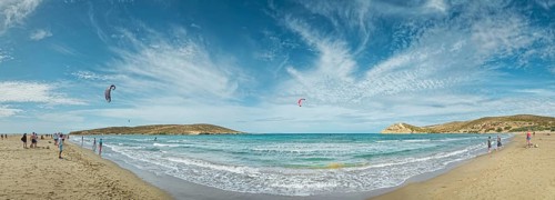 Spacious beach of Prasonisi with light sand, blue sea and two kite surfers under a cloudy sky,