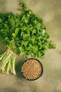 A bundle of fresh cilantro sits neatly tied, next to a small bowl filled with coriander seeds. The