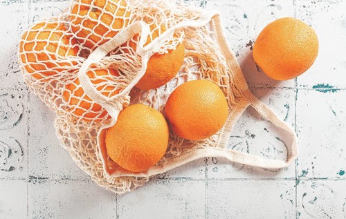 Oranges in a mesh bag, on a textured surface, sunlight, no people