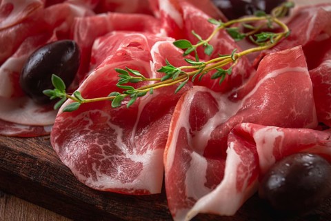 Freshly cut dried meat, served with olives and herbs, on a wooden chopping board, no people