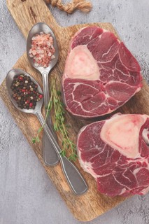 Freshly sliced beef legs, two ossobuco steaks, on a wooden board, with spices and herbs, ready to