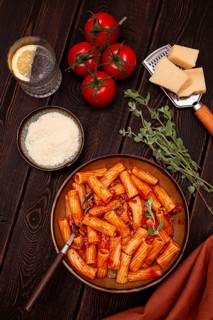Rigatoni pasta with meat sauce and parmesan cheese on a dark wood table with ingredients, top view