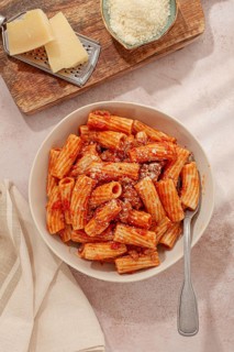 Rigatoni pasta with meat sauce and parmesan cheese on a light table, top view, homemade, no people