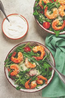 Two bowls of shrimp salad, arugula and cherry tomatoes, with parmesan cheese, healthy food