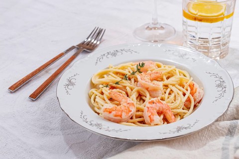 Pasta with shrimp and thyme, served on a white plate, with a glass of white wine, the table is set,