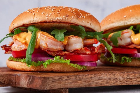 Two shrimp burgers and buns with sesame seeds, bacon, lettuce, tomatoes and onions, On a wooden