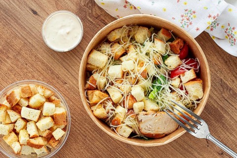 Caesar salad in a paper container, take it on the way, with sauce and croutons, on the table,