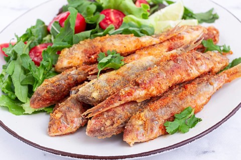 Fried crispy mullet fish, with fresh salad, on a plate with lime, no people