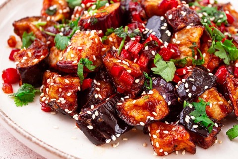 Fried eggplant, Chinese style, in sweet and sour sauce, with pepper and sesame seeds. on a white
