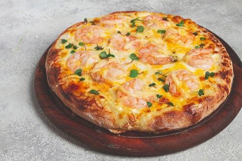 Four cheese pizza with shrimp and fresh microgreens, served on a wooden board, homemade, no people
