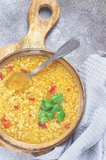 A nourishing bowl of lentil soup filled with grains and vibrant red pepper pieces sits on a