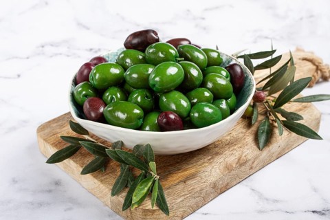 Chalkidiki olives, classic Greek green olives, in a bowl on a cutting board, top view, without