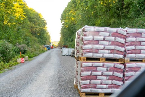 Stacked pallets of building materials line a gravel road in the forest, Hermann Hessebahn