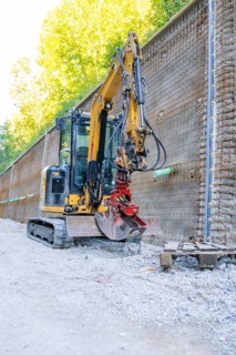 Mini excavator next to a metal mesh construction wall on a building site, Hermann Hessebahn