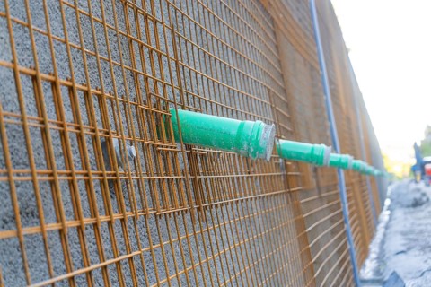 Metal grid with green pipes in front of a concrete wall on a construction site, Hermann Hessebahn