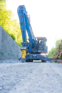 Blue excavator with hydraulic hammer on a path on a concrete wall, Hermann Hessebahn construction