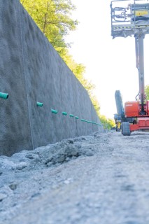 Concrete wall along a road with exposed earth and equipment on a construction site, Hermann