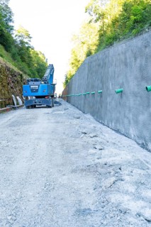 Construction site scene with blue crane next to a high concrete wall and gravel path, Hermann