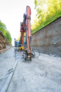 Excavator in action on a construction site next to a concrete wall with pipes, Hermann Hessebahn