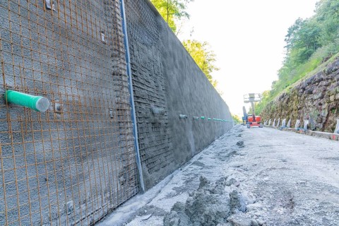 Long concrete wall with reinforcements along a construction site surrounded by trees, Hermann
