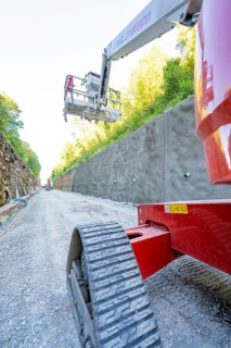 Red lifting platform on a gravel path in front of a concrete wall in the sunshine, Hermann