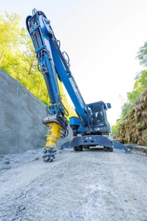 Blue crane with drill head on construction site on concrete wall, surrounded by nature, Hermann