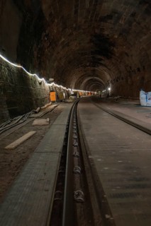 Long stone tunnel with lighting and construction equipment along the track, construction of the