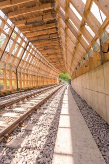 Wooden tunnel structure over railway tracks, bright sunlight floods the room, construction of the