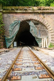 Railway tunnel with rails and stone wall, surrounded by green plants, renovation work in progress,