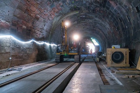 A large machine is used for construction work in the structured tunnel. Rails and wood are visible,