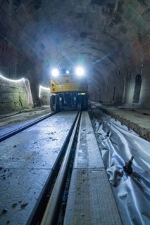 A yellow vehicle with bright lights stands in the tunnel, the rails are visible, construction of