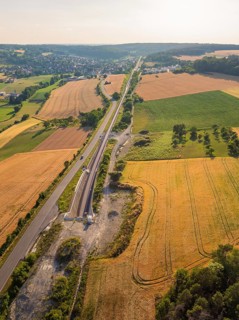 Fields and tracks, running parallel to a road, surrounded by trees, with a view of a distant