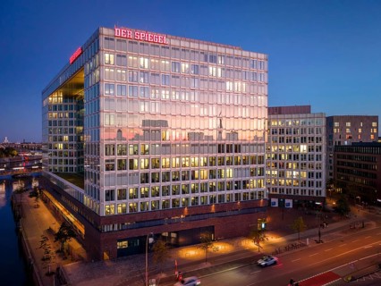 Aerial view of the Spiegel building with glass façade and illuminated offices at blue hour,