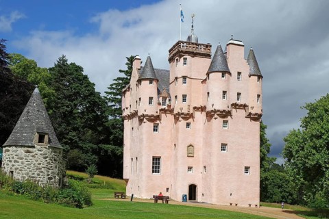 Pink castle with turrets and banner in a meadow under a cloudy sky, Craigievar Castle,