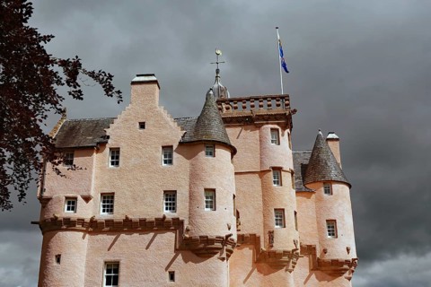 Pink castle with towers and banner in front of a threatening, cloudy sky, Craigievar Castle,