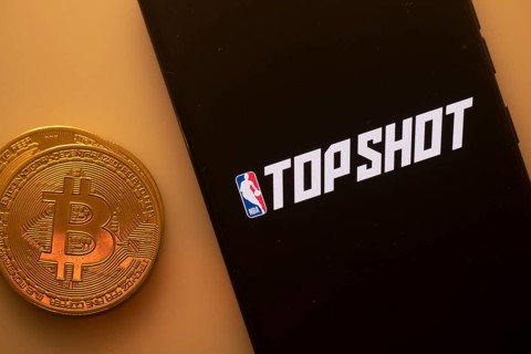 A Bitcoin and Top Shot logo on a black screen representing cryptocurrency