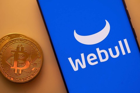 Bitcoin coin next to a smartphone showing Webull logo on a blue background