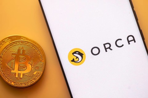 Bitcoin coin beside smartphone with Orca logo on a white screen