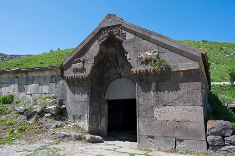 An old stone building with reliefs and a large entrance surrounded by green hills, Selim