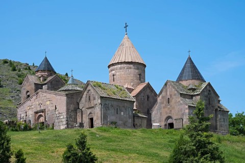 An old monastery with several towers and cross-decorated roofs on a green hill under a clear blue