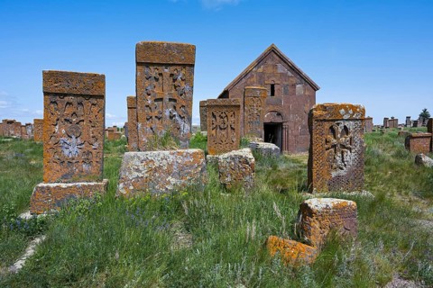 Old gravestones and a chapel in a green cemetery under a bright blue sky, cross stones, the world's